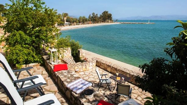 A stone patio with outdoor seating, a view of a beach, and a clear blue sea. - Seafront apartment ΙΙ in Kiveri, near Nafplion. (kiveri)