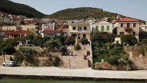 A coastal town with stone buildings, a white car parked by the waterfront, and a hill in the background. - Seafront apartment ΙΙ in Kiveri, near Nafplion. (kiveri)