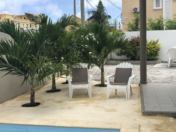 Uma área de pátio com cadeiras brancas e uma pequena piscina.
