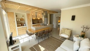 Een moderne keuken met een centraal eiland, houten keukenkastjes en een eethoek met rieten stoelen.