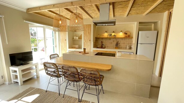 Een moderne keuken met een houten kookeiland, barstoelen en een televisie op een witte standaard.