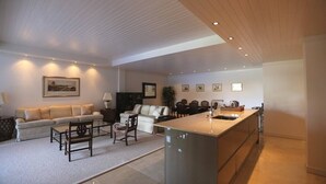 A modern living room with a sofa, coffee table, and chairs, a kitchen with a large island, and a dining area with chairs and a table.
