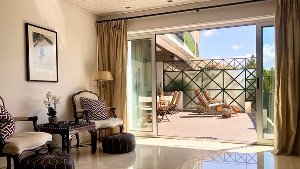 A spacious living area with a modern design, featuring a large sliding glass door leading to an outdoor patio with seating.