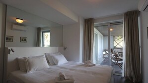 A hotel room with a large bed, a mirror, a window with curtains, and a view of the outdoor seating area.