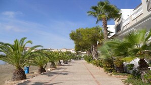 A coastal walkway lined with palm trees and buildings, leading to a beach. - Beautiful house in La Manga The pedruchillo. First line beach garage and pool (San Javier)