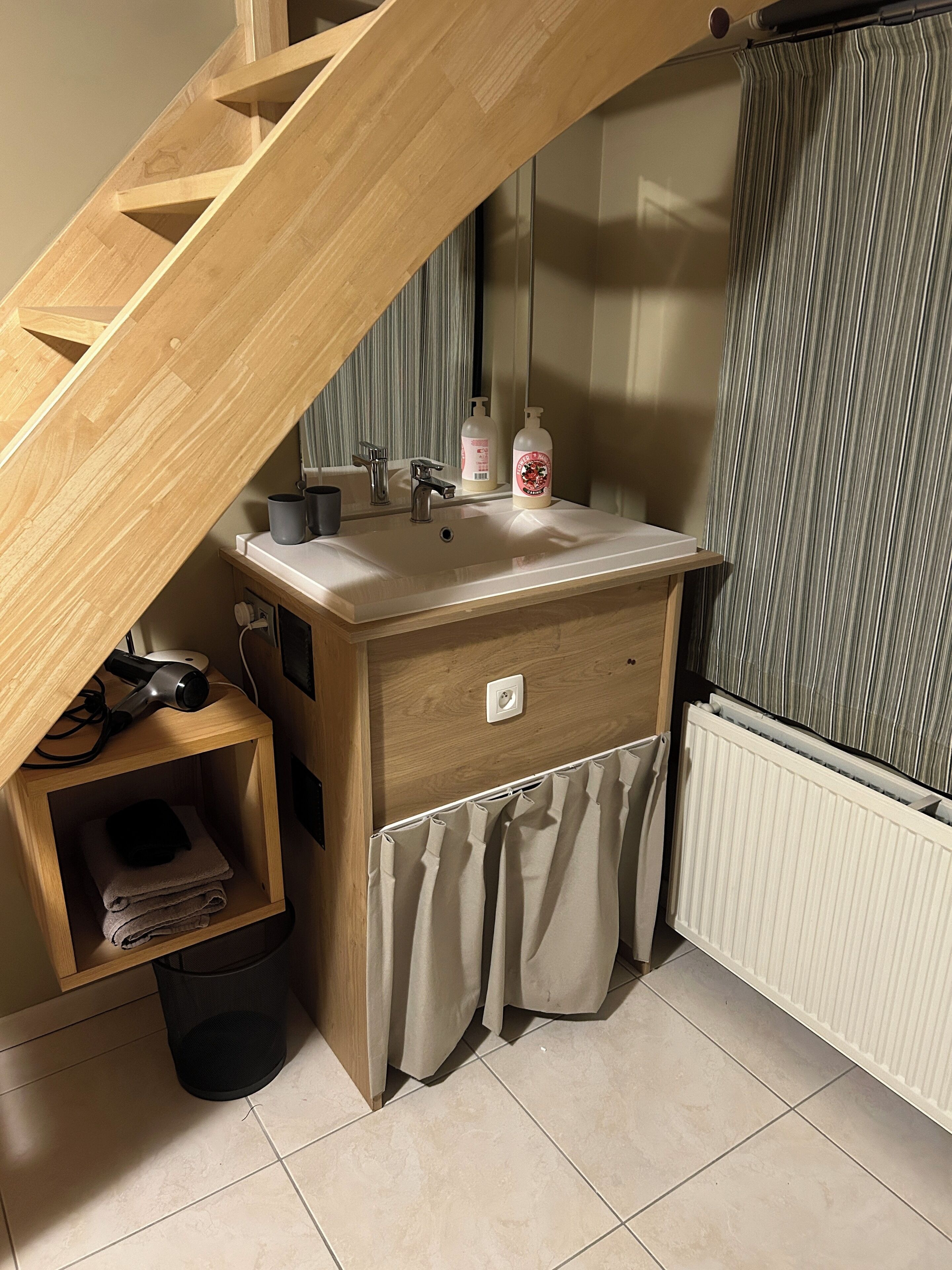 Et badeværelse med en trætrappe, et håndvaskspejl, et håndklædetørrestativ og en radiator.