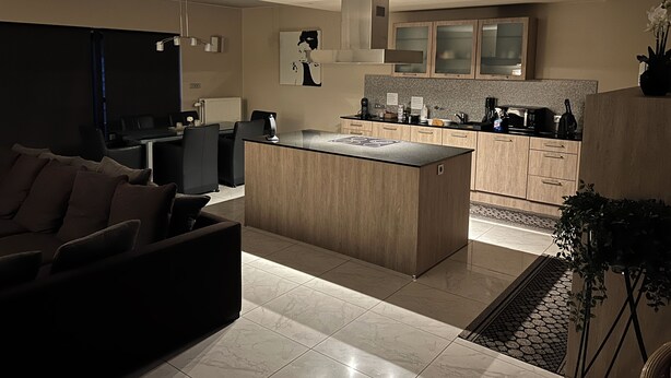 Een moderne keuken met een centraal eiland, houten kastjes en een zithoek met een donkerblauwe bank.