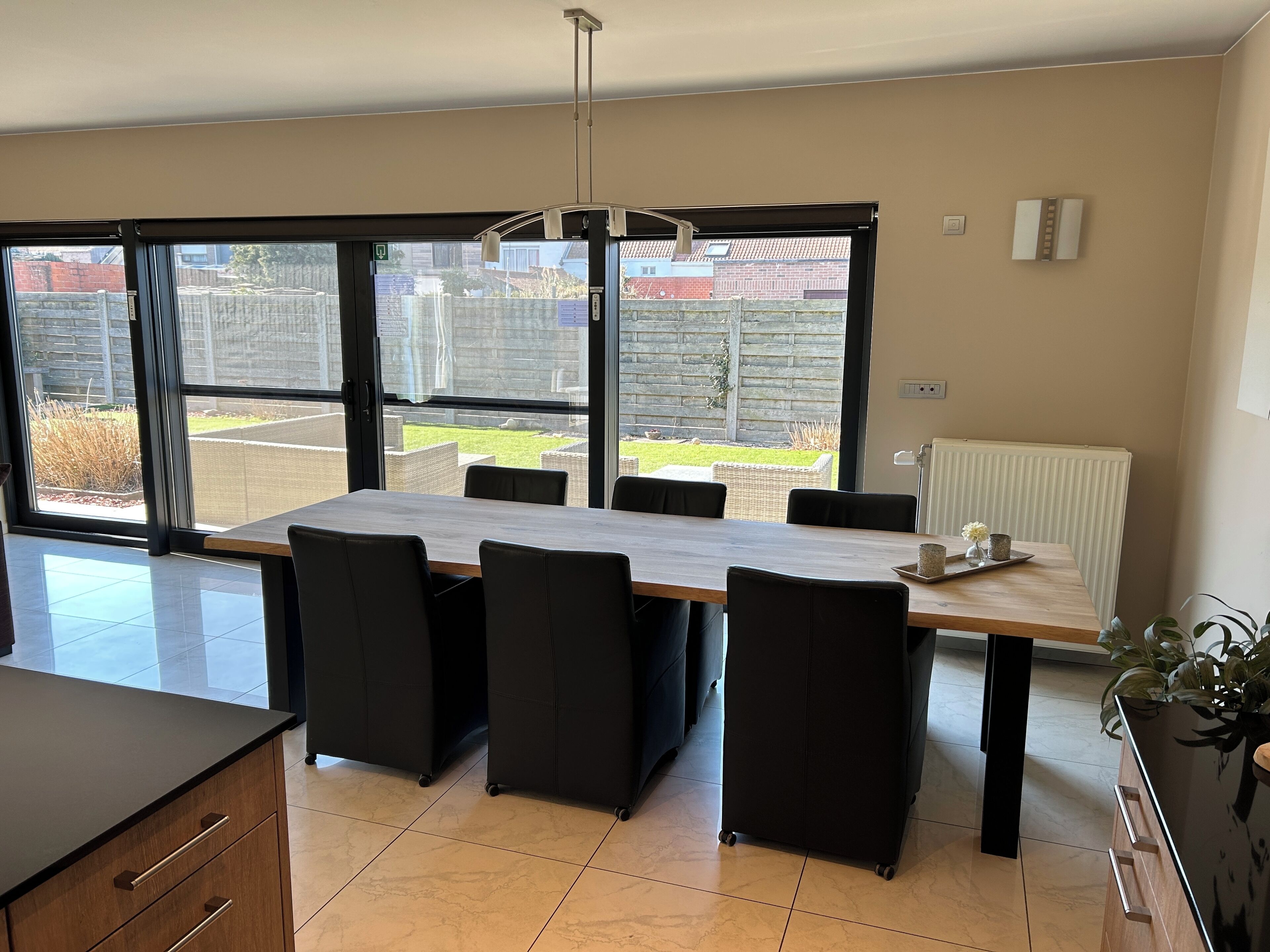 A modern kitchen with a large dining table, black chairs, and a view of the backyard through large windows.