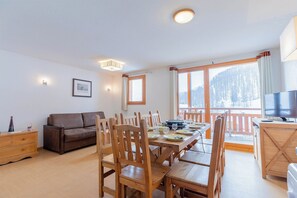 A furnished room with a dining table, chairs, a sofa, a television, and a view of a snowy landscape.