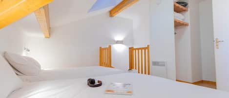 A bedroom with a sloped ceiling, a bed with white bedding, a wooden headboard, a nightstand, a wall-mounted lamp, and a door with a towel rack.