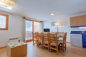 A cozy room with a dining table, chairs, a television, and a kitchen area.