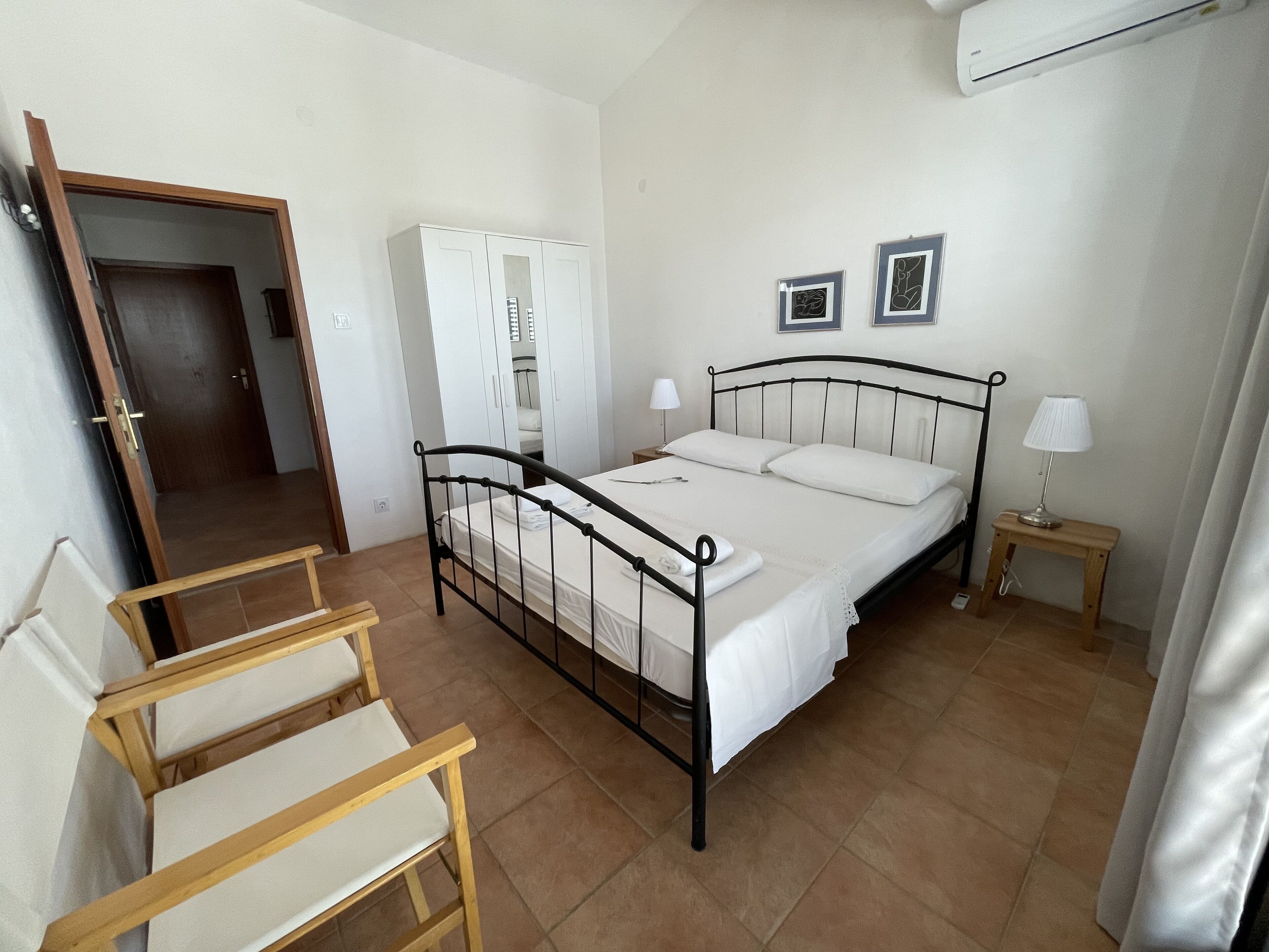 Quarto com cama, cadeiras de madeira, guarda-roupa, mesa de cabeceira e abajur.