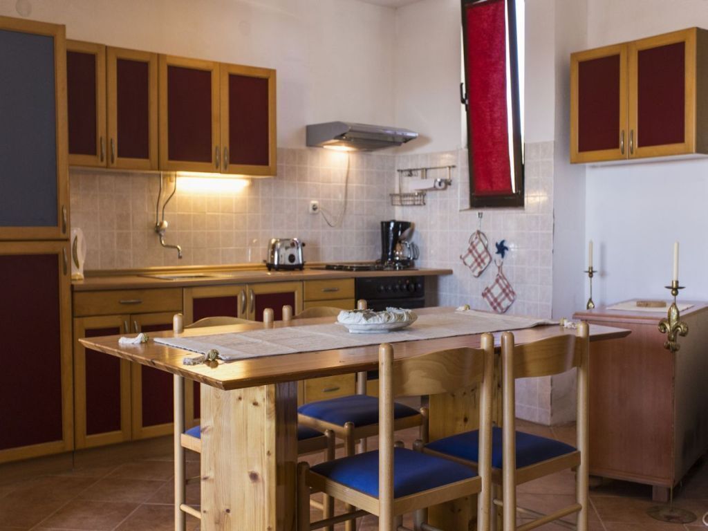 Una cucina compatta con mobili in legno, un fornello a gas e un piccolo tavolo da pranzo con sedie blu.
