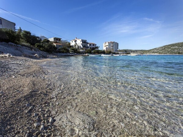 A coastal area with clear shallow waters, rocky beach, and buildings on the hillside. - SPECIAL PRICES!! Stunning Sea View from Terrace in Peaceful Area (Rogoznica)