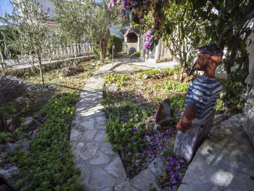 A garden pathway with stone paving, surrounded by greenery and purple flowers.