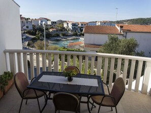 A balcony with a table and chairs, overlooking a coastal town with buildings and a beach. - SPECIAL PRICES!! Stunning Sea View from Terrace in Peaceful Area (Rogoznica)