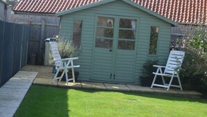 A small, light green wooden shed with a tiled roof, two white folding chairs, and a well-maintained lawn. - Fuzzy Duck Cottage. Over 100 5 star reviews on Trip Advisor. Sleeps 4  (Heacham)