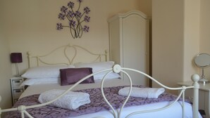 A neatly made bed with white and purple linens, a bedside lamp, and a wall-mounted mirror. - Fuzzy Duck Cottage. Over 100 5 star reviews on Trip Advisor. Sleeps 4  (Heacham)