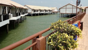 Bungalows sobre el agua con balcones, unidos por una pasarela, y una extensión de agua al frente.