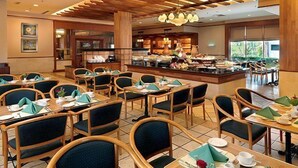 Un comedor con varias mesas y sillas, un mostrador de buffet y vistas al exterior.