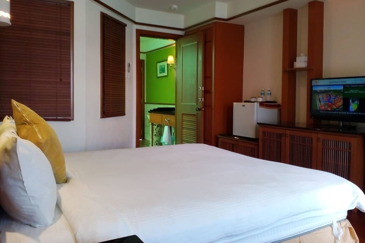 A hotel room with a bed, a television, and a green door leading to another room.