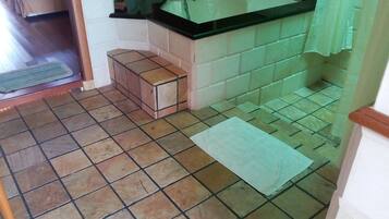 Een badkamer met een wastafel, betegelde vloer en een klein bankje.