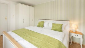 Un letto rifatto con cura, una coperta verde, un comodino con una lampada e un armadio con una maniglia.