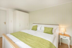 A neatly made bed with a green throw, a bedside table with a lamp, and a wardrobe with a door handle. - Cozy vacation apartment in Ahlbeck with terrace, 500 m to the beach (Seebad Ahlbeck)