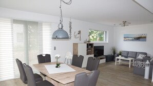 A modern living room with a wooden dining table, grey chairs, a grey sofa, and a fireplace.