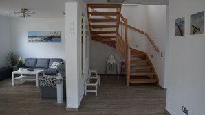 A modern living room with a wooden staircase, a grey sofa, a white coffee table, and a painting on the wall.