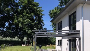A modern house with a covered patio, a barbecue grill, and a fenced garden area.