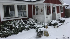 Une maison rouge et blanche avec un porche, recouverte de neige, et un drapeau suédois.