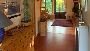 Un hall spacieux avec un plancher en bois, une commode en bois dotée de tiroirs, un tableau encadré et une plante en pot.