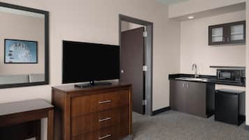 A hotel room with a wooden dresser, a flat-screen TV, a microwave, a sink, and a door leading to another room.