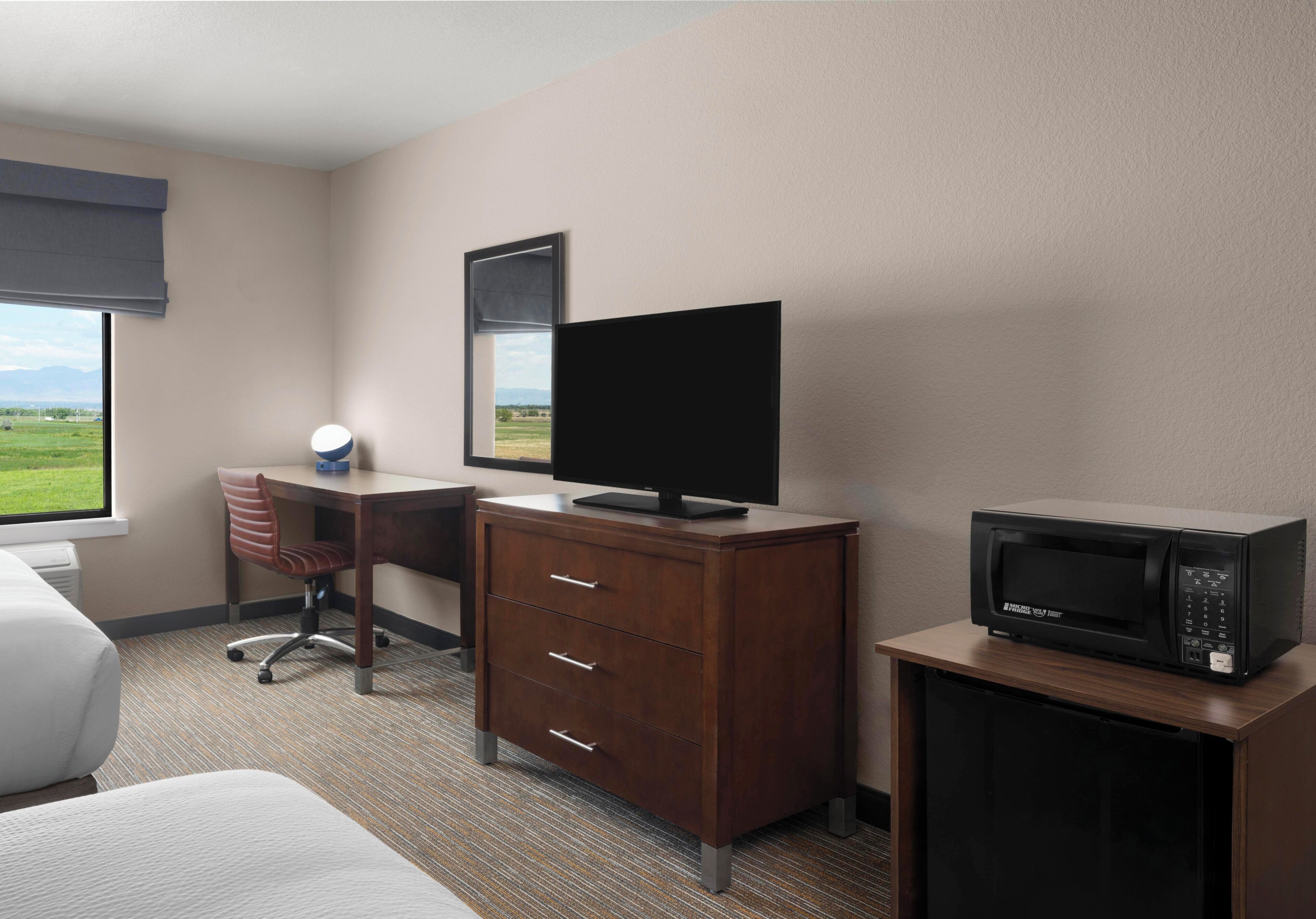 A hotel room with a bed, a desk with a chair, a dresser, a television, and a microwave.