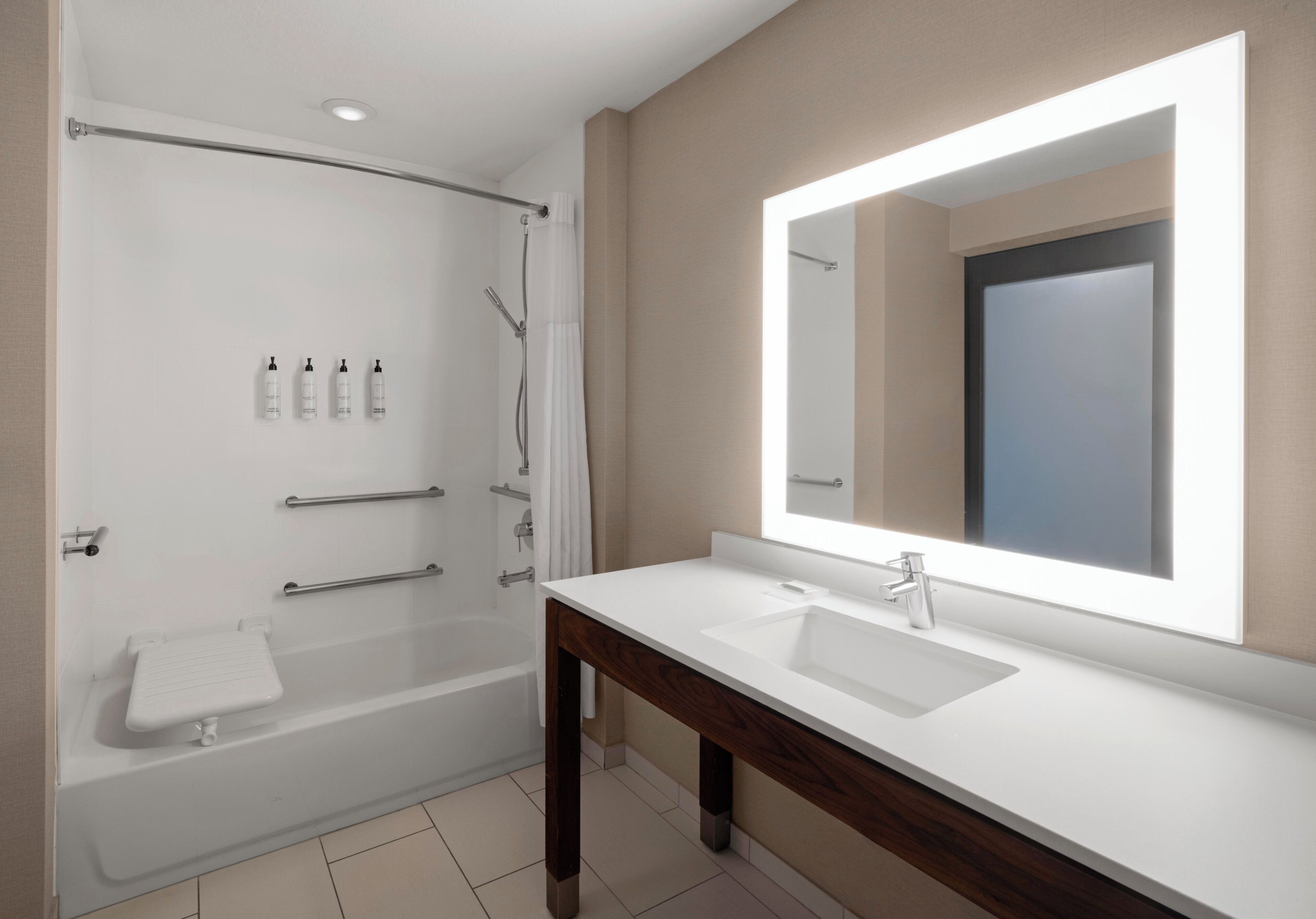 Un baño moderno con bañera, ducha y un espejo grande sobre el lavabo.