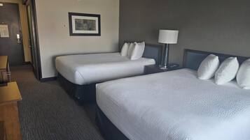 Habitación de hotel con dos camas, una mesita de noche con lámpara, un cuadro en la pared y piso alfombrado.