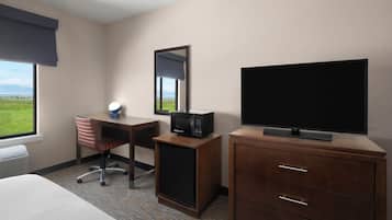 A hotel room with a bed, a desk with a chair, a television, a small refrigerator, and a mirror.