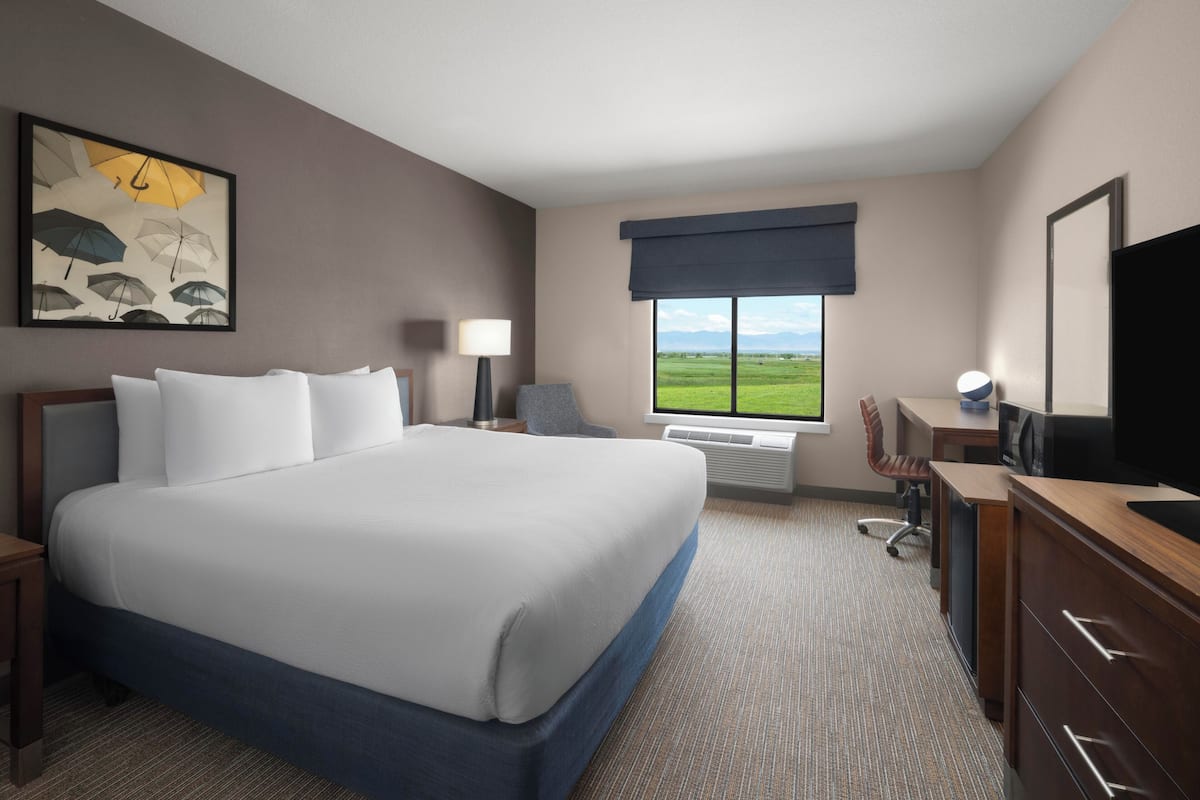Ein Hotelzimmer mit einem großen Bett, einem Schreibtisch mit Computer, einem Sessel, einem Fernseher und einem Fenster mit Ausblick ins Freie.