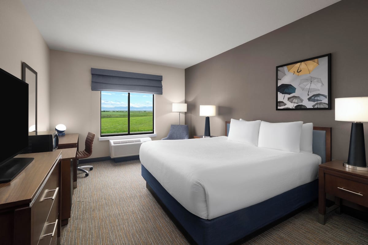 Ein Hotelzimmer mit einem großen Bett, einem Schreibtisch mit Computer, einem Sessel, einem Fernseher und einem Fenster mit Blick ins Freie.