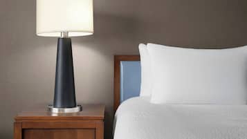 A bed with white bedding, a wooden nightstand with a lamp, and a wall with a textured finish.