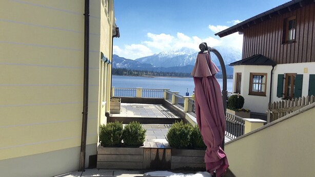 A building with a balcony overlooking a lake and mountains. - 5 star apartment on Lake Hopfensee directly on the lake with 2 terraces & underground parking space (Hopfen am See)