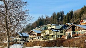 A snow-covered landscape with a row of chalet-style buildings, each with a balcony and a sloped roof. - 5 star apartment on Lake Hopfensee directly on the lake with 2 terraces & underground parking space (Hopfen am See)