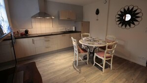 Une cuisine moderne avec des meubles en bois, une hotte de cuisine en acier inoxydable et un coin repas comprenant une table ronde et des chaises blanches.