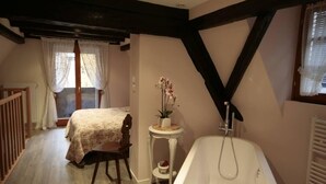 Une chambre à coucher avec un lit, une petite table sur laquelle est posée une plante en pot, une baignoire et une fenêtre avec des rideaux.