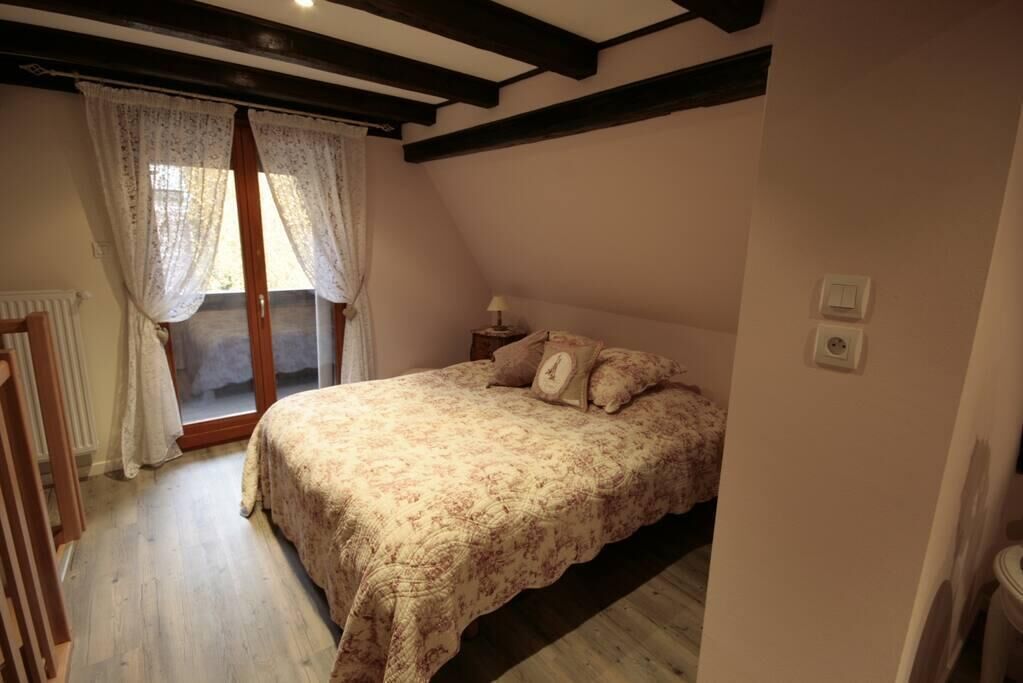 A bedroom with a bed, a window with curtains, a radiator, and a wooden floor.
