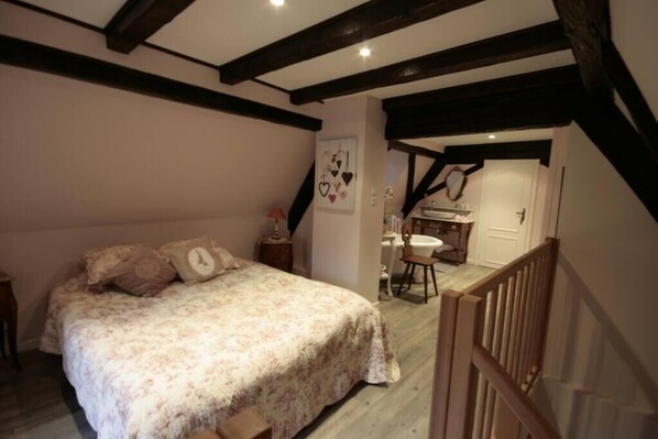Un dormitorio con cama, mesita de noche, pared decorada con corazones y una escalera que lleva a un baño.