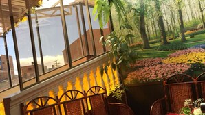A conservatory with wicker chairs and red cushions, a glass wall with a view of a garden and buildings. - Gran Copacabana Hostal (El Alto)