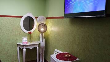 Una habitación con una pared verde, una mesa blanca con un espejo y un objeto decorativo, un televisor instalado en la pared y un radiador blanco.