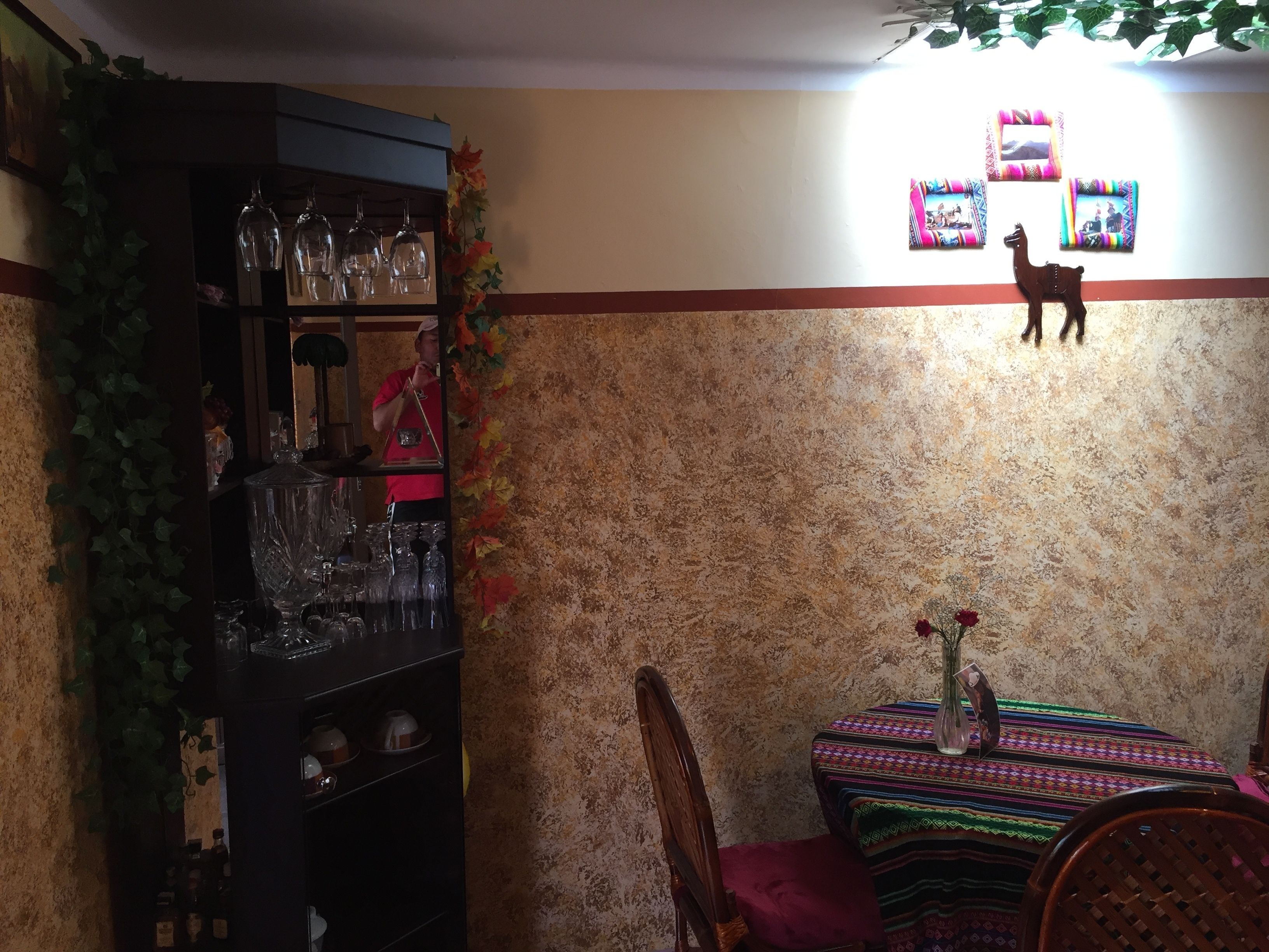 A dining area with a table set for two, a bar area with glassware, and a wall decorated with framed photos and a small statue.
